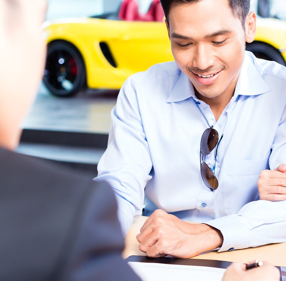 Man signing a deal with a yellow sports car in the background